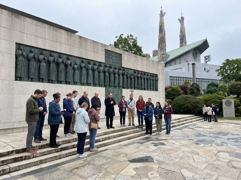 Catholic pilgrimage group praying beside the Twenty-Six Martyrs Monument at Nishizaka Hill in Nagasaki